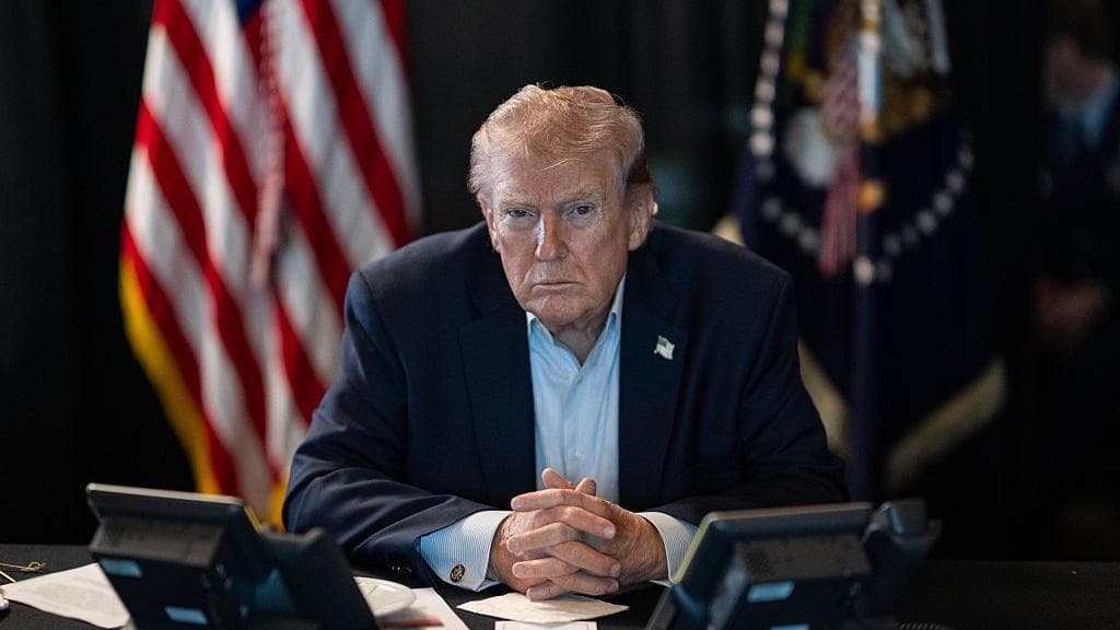 President Trump seated at a command table flanked by US and presidential flags during the Iran military operation briefing